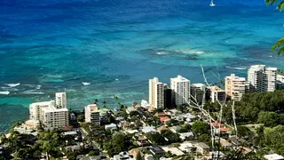 Turquoise ocean water stretches beyond a dense cluster of coastal high-rise buildings and houses.