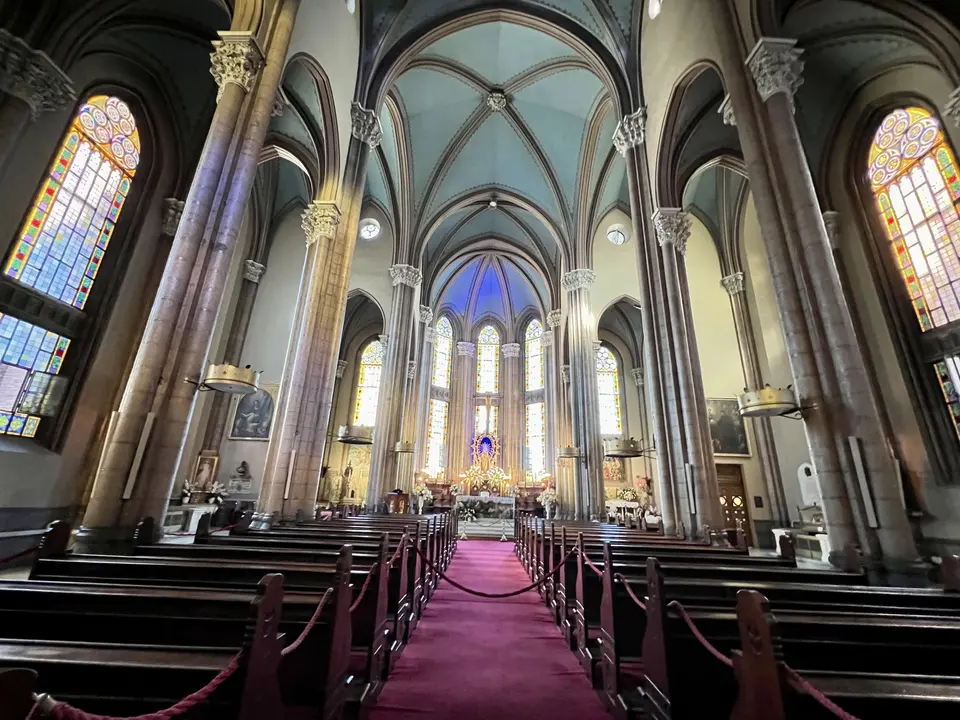 The vaulted interior of St. Anthony of Padua Church features tall stone columns, stained-glass windows, wooden pews, and a red-carpeted central aisle leading to the altar.