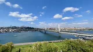 The Golden Horn Metro Bridge spans the water beneath a bright blue sky, with Istanbul's densely built hills and mosque minarets behind it.
