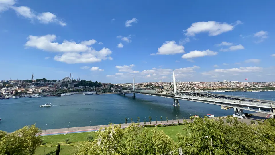 The Golden Horn Metro Bridge spans the water beneath a bright blue sky, with Istanbul's densely built hills and mosque minarets behind it.