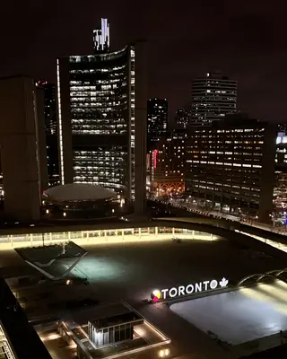 Toronto City Hall and surrounding illuminated office towers overlook the glowing TORONTO sign at night.