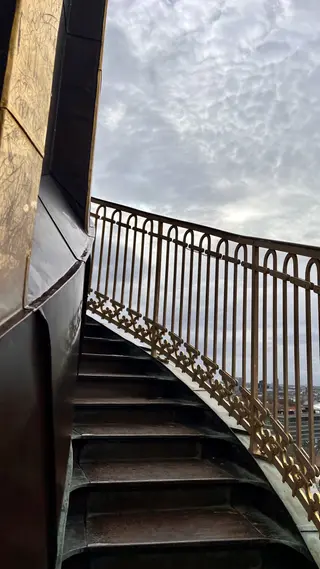 The exterior spiral staircase of Copenhagen's Church of Our Saviour rises beside an ornate metal railing beneath a cloudy sky.