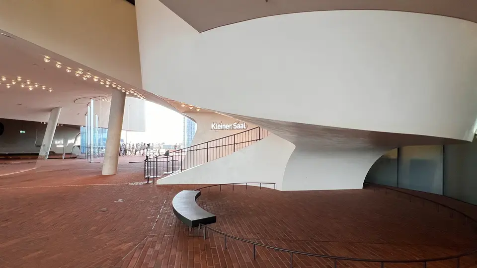 The sweeping white interior of the Elbphilharmonie features brick flooring, curved railings, and a staircase marked “Kleiner Saal.”