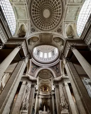 The ornate vaulted interior of the Panthéon features coffered domes, skylights, towering fluted columns, and sculptural reliefs.