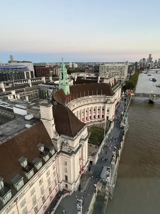 London County Hall curves along the River Thames beside Westminster Bridge, with pedestrians on the riverside walkway and modern buildings beyond.