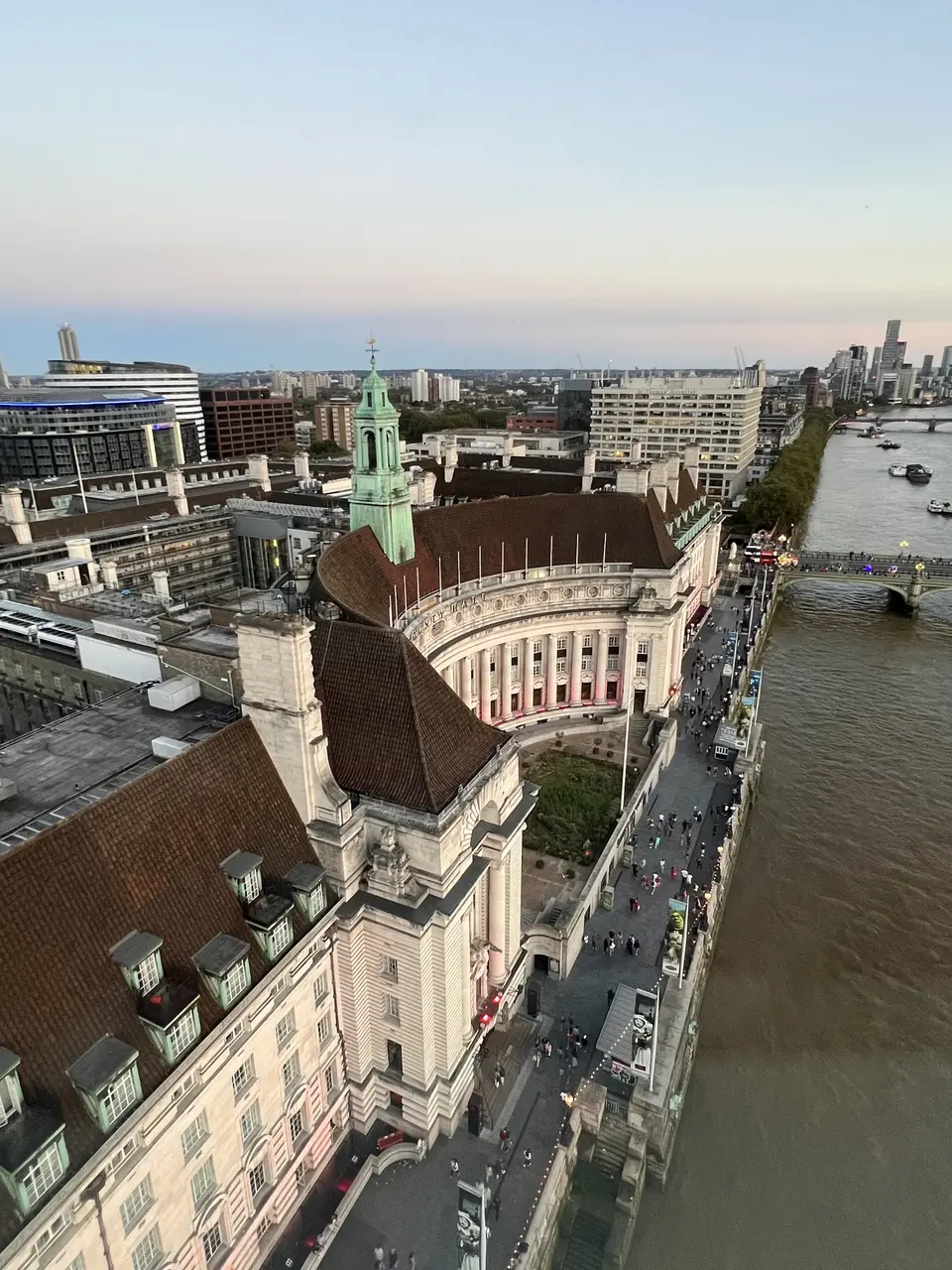 London County Hall curves along the River Thames beside Westminster Bridge, with pedestrians on the riverside walkway and modern buildings beyond.