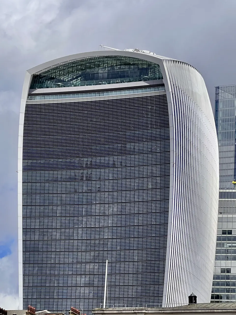 The distinctive curved facade of 20 Fenchurch Street, known as the Walkie Talkie, rises beneath a cloudy sky.