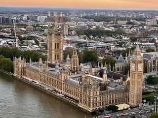 An aerial view of the Palace of Westminster and Elizabeth Tower beside the River Thames at sunset.