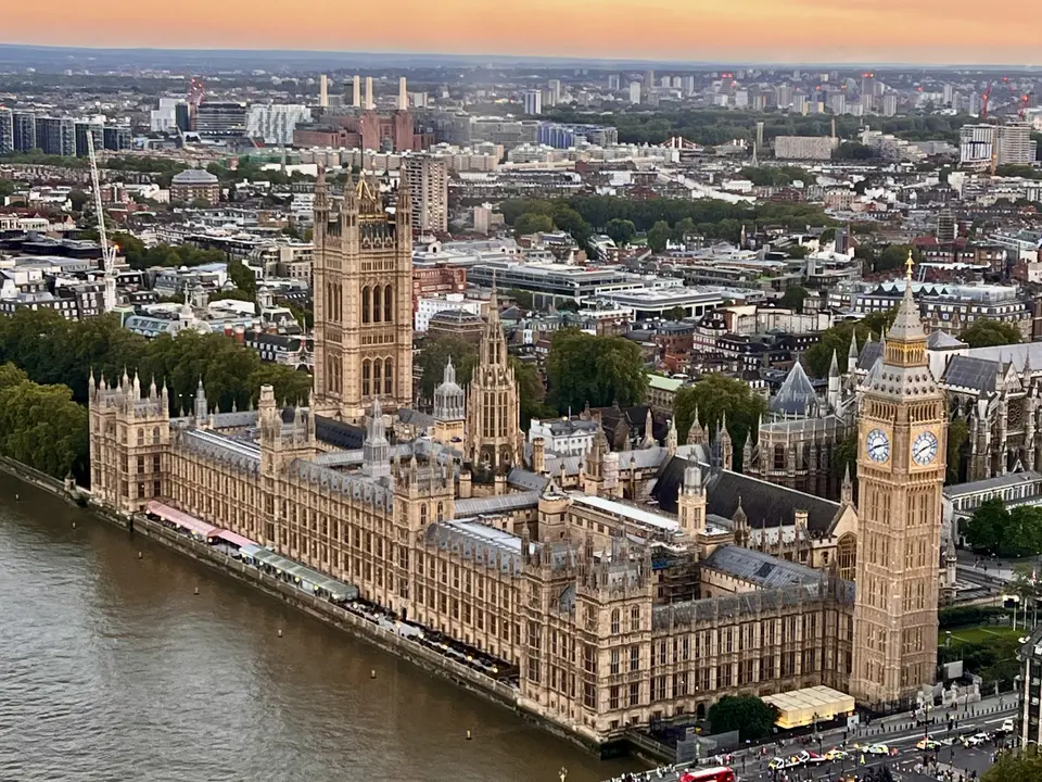 An aerial view of the Palace of Westminster and Elizabeth Tower beside the River Thames at sunset.