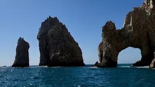 El Arco de Cabo San Lucas rises beside rugged sea stacks above turquoise ocean water under a clear blue sky.