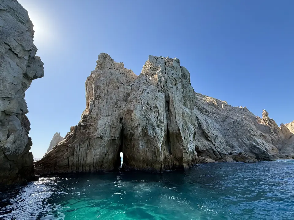 El Arco de Cabo San Lucas rises above clear turquoise water beneath a cloudless blue sky.
