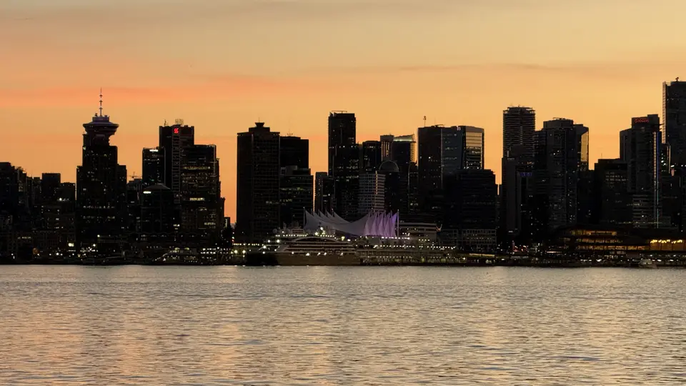Vancouver's waterfront skyline glows at sunset behind Canada Place and calm harbor water.