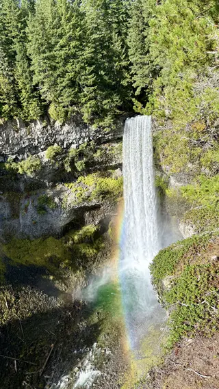 Brandywine Falls plunges over a rocky, forested cliff into a misty pool beneath a bright rainbow.