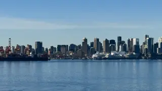 Vancouver’s waterfront skyline, including the sail-like roof of Canada Place, rises beyond calm blue water and cargo cranes.