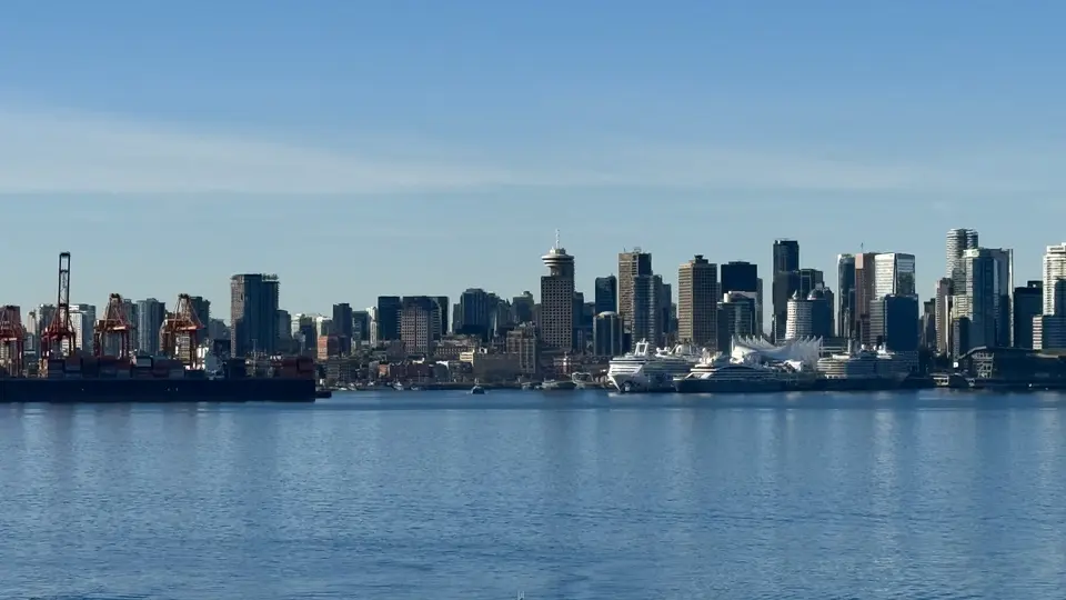 Vancouver’s waterfront skyline, including the sail-like roof of Canada Place, rises beyond calm blue water and cargo cranes.