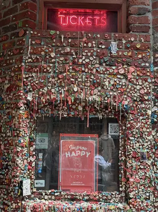 Seattle Gum Wall is covered in colorful chewing gum around a ticket window with a glowing red "TICKETS" sign.