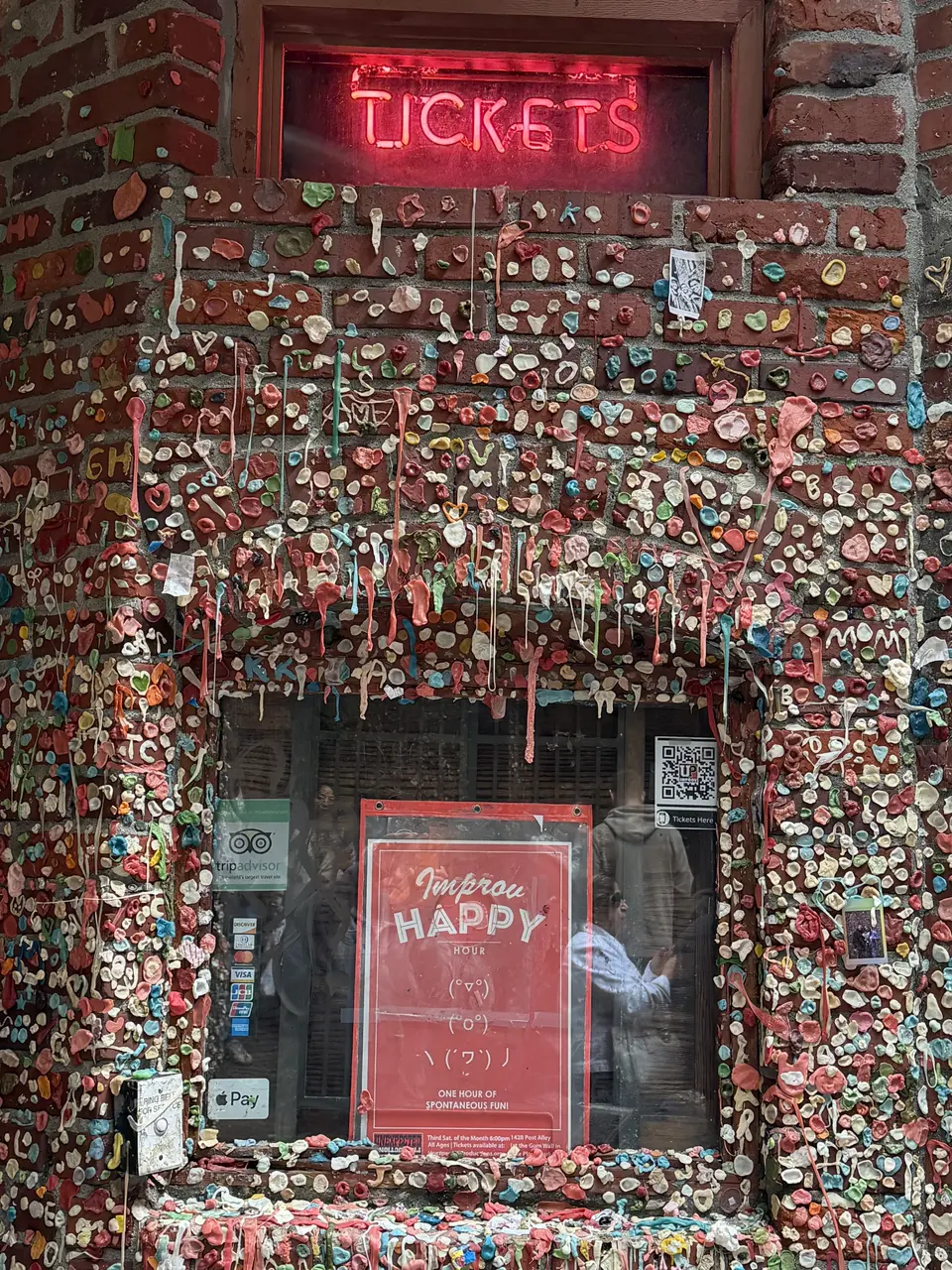 Seattle Gum Wall is covered in colorful chewing gum around a ticket window with a glowing red "TICKETS" sign.