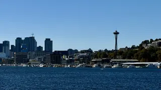 Seattle's skyline and the Space Needle rise above a marina along the waterfront under a clear blue sky.